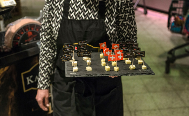 Ein Mann mit einer schwarzen Schürze hält eine schwarze Platte mit kleinen Käsestücken