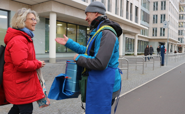 Ein Mann mit einer blauen Tasche steht auf der Straße und unterhält sich mit einer Frau mit einer roten Jacke